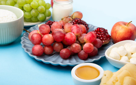 Happy Shavuot holiday card. Jewish religious holiday concept. Dairy products, grapes, cheese, bread, milk, cottage cheese, wheat, honey on blue background.の写真素材