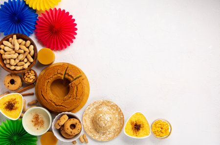 Festa Junina Summer Festival Carnival concept. Brazilian straw hat, Corn Cake, peanuts and colorful flags on white wooden background, top view. Design for Greeting Card, Invitation or Holiday Posterの写真素材