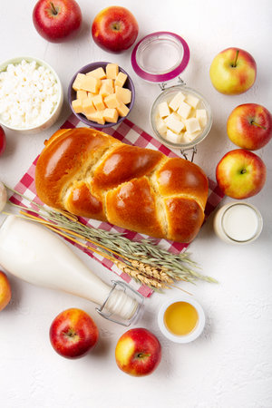 Happy Shavuot holiday card. Jewish religious holiday concept. Dairy products, fresh apples, cheese, bread, milk, cottage cheese, wheat and honey on white background. Top view, copy space.の写真素材