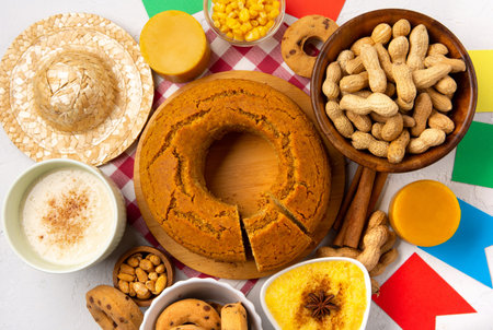 Festa Junina Summer Festival Carnival concept. Brazilian straw hat, Corn Cake, peanuts and colorful flags on white wooden background, top view. Design for Greeting Card, Invitation or Holiday Posterの写真素材
