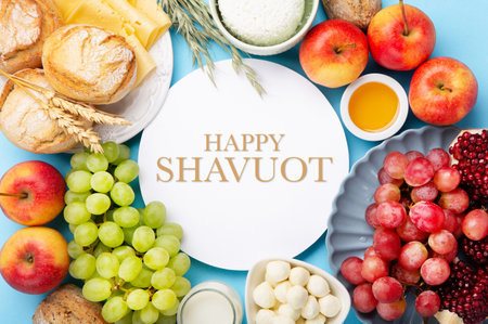 Happy Shavuot holiday card. Jewish religious holiday concept. Dairy products, grapes, cheese, bread, milk, cottage cheese, wheat, honey on blue background. Top view, copy space.の写真素材