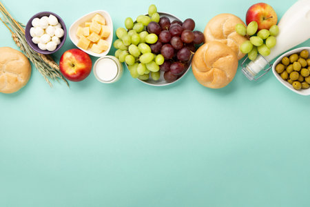 Happy Shavuot holiday card. Jewish religious holiday concept. Dairy products, fruits, cheese, bread, milk bottle, cottage cheese, wheat on blue mint background. Top view, copy space.の写真素材