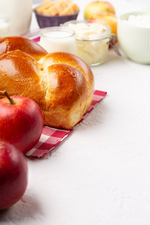 Happy Shavuot holiday card. Jewish religious holiday concept. Dairy products, fresh apples, cheese, bread, milk, cottage cheese, wheat and honey on white background, copy space.の写真素材