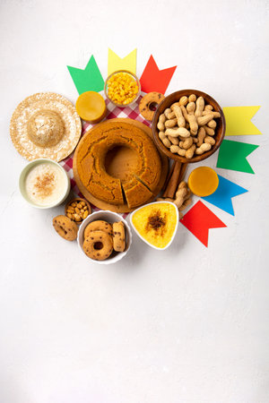 Festa Junina Summer Festival Carnival concept. Brazilian straw hat, Corn Cake, peanuts and colorful flags on white wooden background, top view. Design for Greeting Card, Invitation or Holiday Posterの写真素材