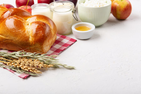 Happy Shavuot holiday card. Jewish religious holiday concept. Dairy products, fresh apples, cheese, bread, milk, cottage cheese, wheat and honey on white background, copy space.の写真素材