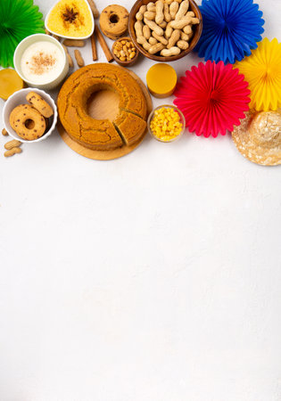 Festa Junina Summer Festival Carnival concept. Brazilian straw hat, Corn Cake, peanuts and colorful flags on white wooden background, top view. Design for Greeting Card, Invitation or Holiday Posterの写真素材