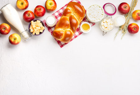 Happy Shavuot holiday card. Jewish religious holiday concept. Dairy products, fresh apples, cheese, bread, milk, cottage cheese, wheat and honey on white background. Top view, copy space.の写真素材