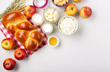 Happy Shavuot holiday card. Jewish religious holiday concept. Dairy products, fresh apples, cheese, bread, milk, cottage cheese, wheat and honey on white background. Top view, copy space.の写真素材
