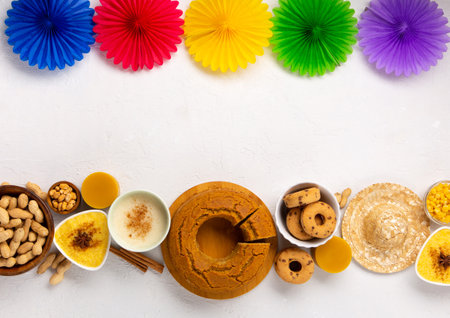 Festa Junina Summer Festival Carnival concept. Brazilian straw hat, Corn Cake, peanuts and colorful flags on white wooden background, top view. Design for Greeting Card, Invitation or Holiday Posterの写真素材