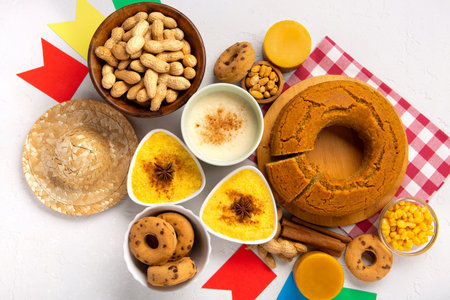 Festa Junina Summer Festival Carnival concept. Brazilian straw hat, Corn Cake, peanuts and colorful flags on white wooden background, top view. Design for Greeting Card, Invitation or Holiday Posterの写真素材