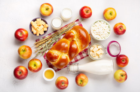 Happy Shavuot holiday card. Jewish religious holiday concept. Dairy products, fresh apples, cheese, bread, milk, cottage cheese, wheat and honey on white background. Top view, copy space.の写真素材