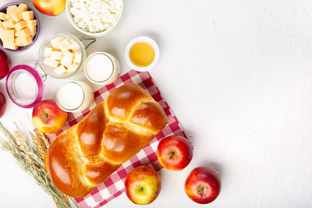 Happy Shavuot holiday card. Jewish religious holiday concept. Dairy products, fresh apples, cheese, bread, milk, cottage cheese, wheat and honey on white background. Top view, copy space.の写真素材