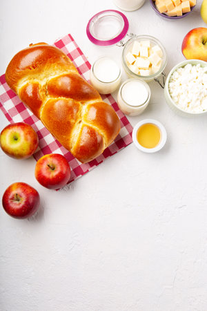 Happy Shavuot holiday card. Jewish religious holiday concept. Dairy products, fresh apples, cheese, bread, milk, cottage cheese, wheat and honey on white background. Top view, copy space.の写真素材