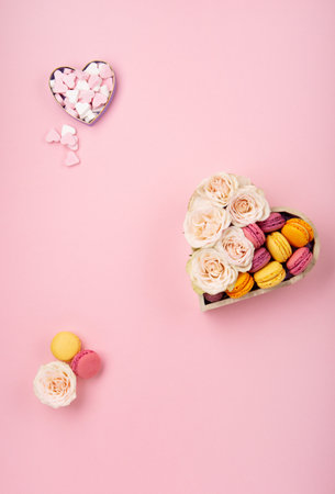 Sweet cookies macaroons in festive gift box, rose flowers and candies on pink background. Holiday presents concept for Mothers day, womans day valentines day, birthday. Top view, copy space.の写真素材