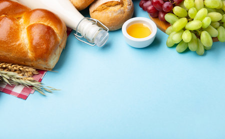 Happy Shavuot holiday card. Jewish religious holiday concept. Dairy products, fresh apples, grapes, cheese, bread, milk, cottage cheese, wheat and honey on blue background, copy space.の写真素材