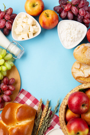 Happy Shavuot holiday card. Jewish religious holiday concept. Dairy products, fresh apples, grapes, cheese, bread, milk, cottage cheese, wheat and honey on blue background. Top view, copy space.の写真素材