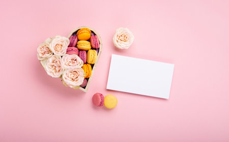 Sweet cookies macaroons in festive gift box, rose flowers and candies on pink background. Holiday presents concept for Mothers day, womans day valentines day, birthday. Top view, copy space.の写真素材
