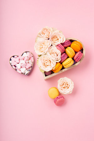 Sweet cookies macaroons in festive gift box, rose flowers and candies on pink background. Holiday presents concept for Mothers day, womans day valentines day, birthday. Top view, copy space.の写真素材
