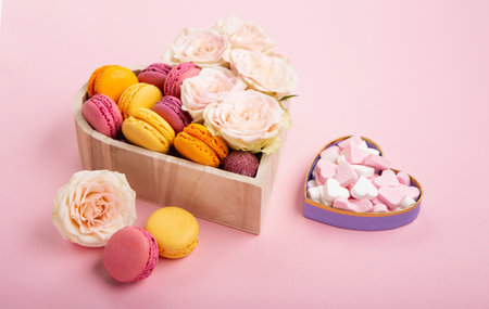 Sweet cookies macaroons in festive gift box, rose flowers and candies on pink background. Holiday presents concept for Mothers day, womans day valentines day, birthday, empty space for text or messageの写真素材