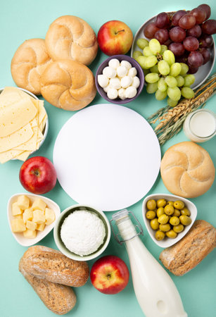 Happy Shavuot holiday card. Jewish religious holiday concept. Dairy products, fruits, cheese, bread, milk bottle, cottage cheese, wheat on blue mint background. Top view, copy space.の写真素材