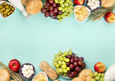 Happy Shavuot holiday card. Jewish religious holiday concept. Dairy products, fruits, cheese, bread, milk bottle, cottage cheese, wheat on blue mint background. Top view, copy space.の写真素材