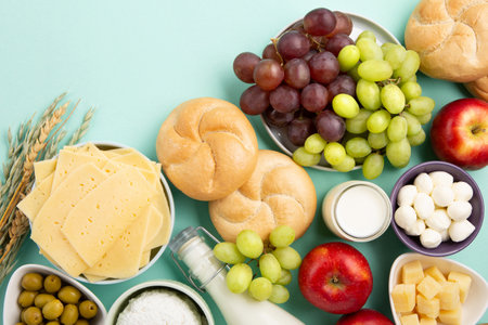 Happy Shavuot holiday card. Jewish religious holiday concept. Dairy products, fruits, cheese, bread, milk bottle, cottage cheese, wheat on blue mint background. Top view, copy space.の写真素材