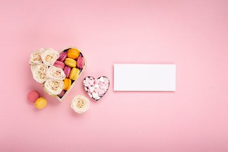 Sweet cookies macaroons in festive gift box, rose flowers and candies on pink background. Holiday presents concept for Mothers day, womans day valentines day, birthday. Top view, copy space.の写真素材