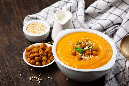 Autumn Vegetarian pumpkin and carrot cream soup with chickpeas and herbs on dark wooden background. Comfort food, fall and winter healthy slow food concept.の写真素材