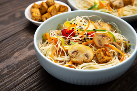 Vegan rice noodles with tofu, peppers, carrots and zucchini prepared for wook on dark brown background. Healthy vegan food conceptの写真素材