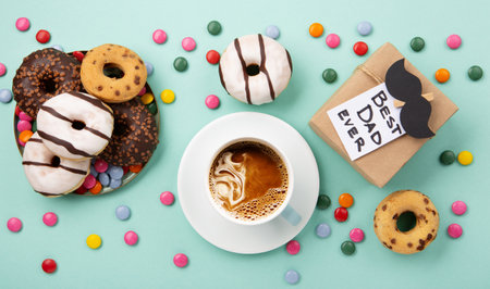Fathers day holiday card concept with craft gift box, black mustache, cup of coffee and donuts or donuts on blue mint background, top view, copy space.の写真素材