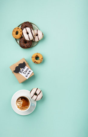 Fathers day holiday card concept with craft gift box, black mustache, cup of coffee and donuts or donuts on blue mint background, top view, copy space.の写真素材