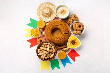 Festa Junina Summer Festival Carnival concept. Brazilian straw hat, Corn Cake, peanuts and colorful flags on white wooden background, top view. Design for Greeting Card, Invitation or Holiday Posterの写真素材