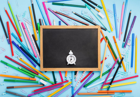 Back to school, Exam, Education concept on blue background. School scattered stationery, notepads, pens, pencils, paper clips and white alarm clock on blue table. Top view, copy space.の写真素材