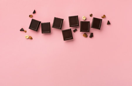 World Chocolate Day, july 07. Dark chocolate bar pieces with nuts on pink background, top view, copy space. Holiday greeting card or banner concept.の写真素材