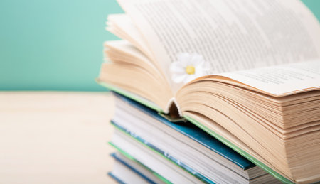 Book Lovers Day, Education concept. Open Book on Stack of books and Daisy Flower on blue mint background. Festive card for books holiday, copy space.の写真素材