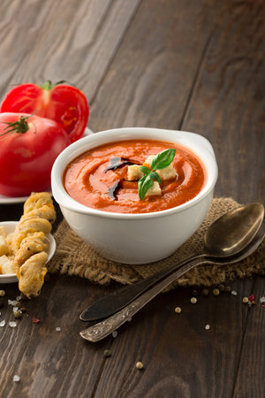 Homemade tomato soup with tomatoes, red pepper, herbs and spices on dark rustic wooden background, selective focusの写真素材