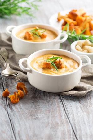 Mushroom cream soup with chanterelles and herbs on a white rustic wooden background, selective focusの写真素材