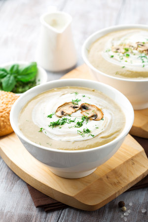 Mushroom cream soup with fried mushrooms and fresh herbs on rustic white wooden table, selective focusの写真素材