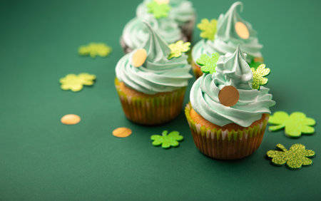 St. Patrick's Day vanilla and chocolate cupcakes with green frosting and shiny clover decorations on green paper background. Irish holiday dessert concept, copy space.の写真素材