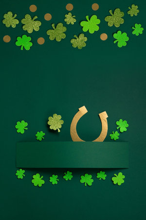 St. Patrick's Day celebration Card. Holiday concept with traditional Irish symbols - Golden horseshoe, gold coins and clover leaves, green shamrocks on green background, copy space.の写真素材