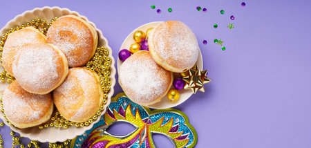 Festive donuts donuts with Mardi Gras Beads, masquerade festival carnival mask and purple, gold, green decor on purple background. Holiday party invitation, greeting card concept.の写真素材