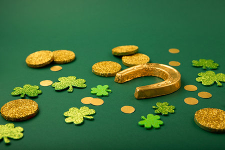 St Patricks day card with traditional symbols for irish party. Golden horseshoe, gold coins, clover leaves, green shamrocks on green background, copy space. St. Patrick's Day celebration concept.の写真素材