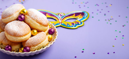 Festive donuts or donuts with Mardi Gras Beads, masquerade festival carnival mask and purple, gold, green decor on purple background. Holiday party invitation, greeting card concept.の写真素材