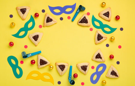 Chocolate dipped hamantaschen cookies, Carnival mask, noisemaker, sweet candies and festive party decor on yellow background, Top view. Purim celebration jewish holiday concept.の写真素材