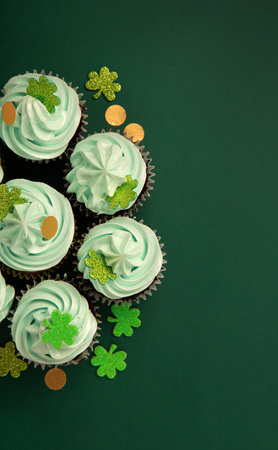 St. Patrick's Day festive vanilla chocolate cupcakes with green frosting and shiny clover decorations on green paper background. Irish holiday dessert concept. Top view, copy space.の写真素材