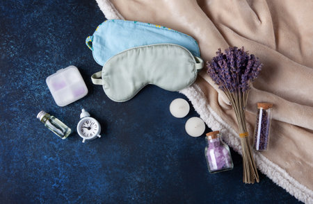 World Sleep Day concept. Bedtime accessories, sleep masks, and classic alarm clock on dark blue wooden backgroundの写真素材