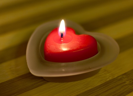 Heart-shaped candle with flame on a wooden surfaceの写真素材