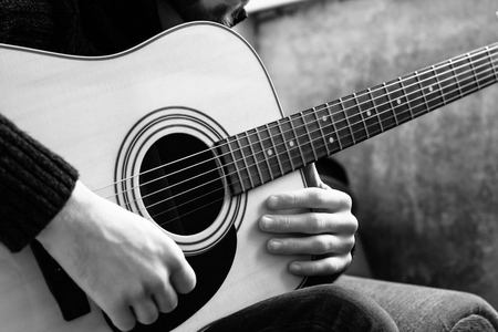 young man playing an acoustic guitar on the background of a concrete wall.の写真素材