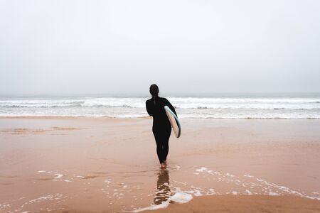 Young girl server stands with a surfboard by the ocean. stormy weather.の写真素材