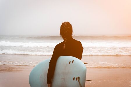 Young girl server stands with a surfboard by the ocean.の写真素材